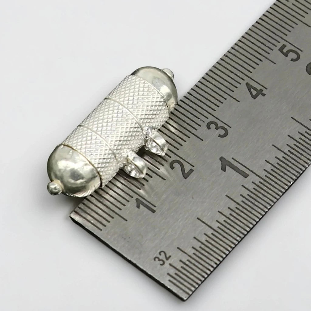 Silver tabiz locket on a metal ruler for measurement