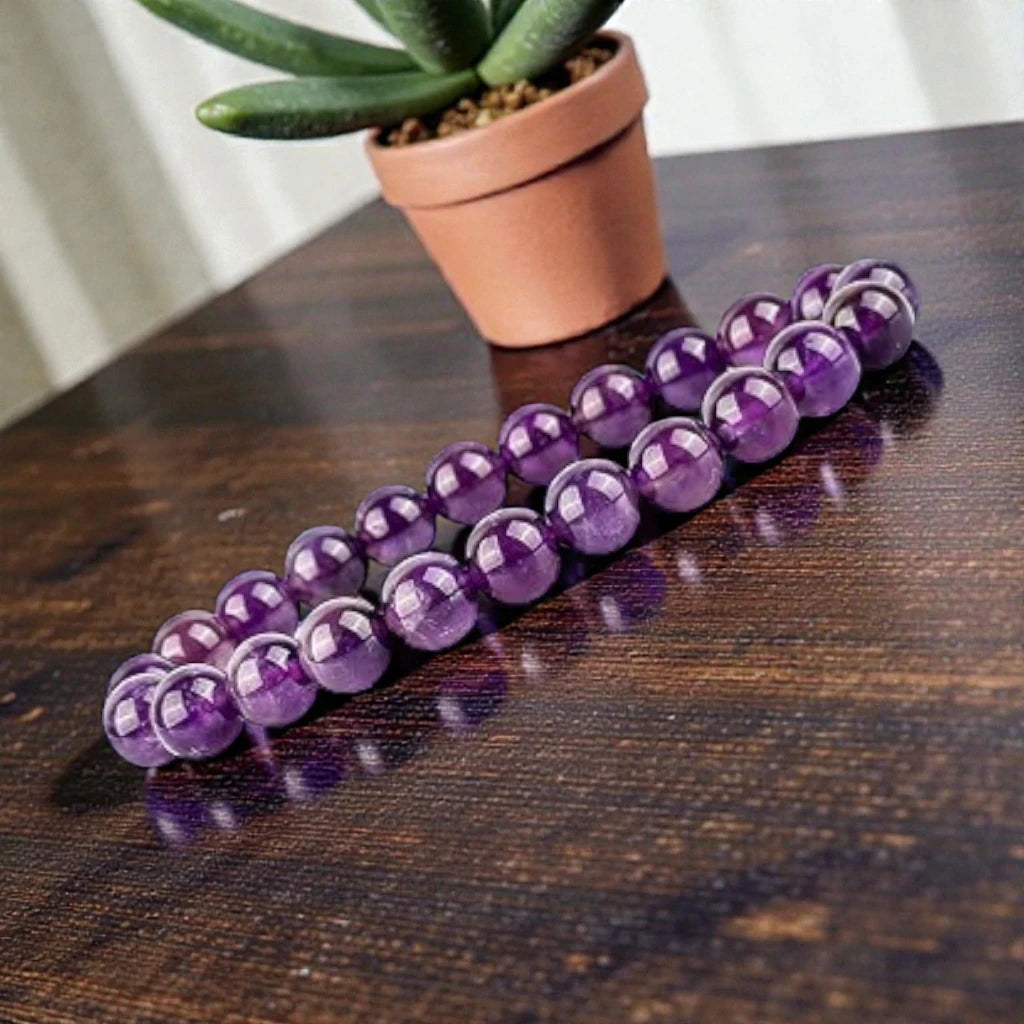 Purple amethyst bracelet on a wooden surface with a potted plant in the background