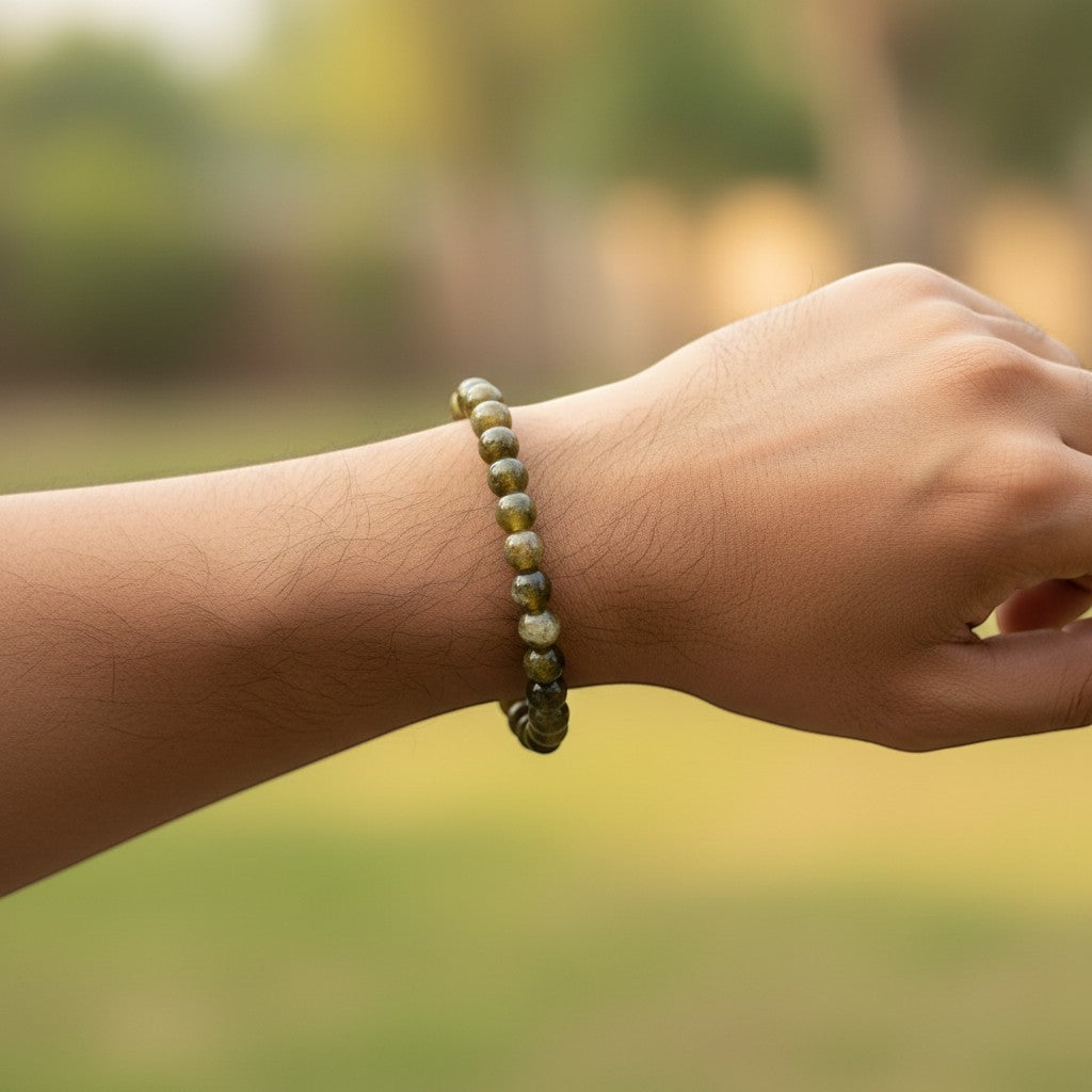 Hand wearing a green tourmaline beaded bracelet with a blurred natural background