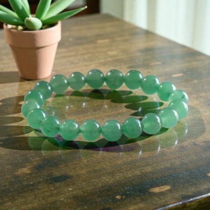 Green Jade bracelet on a wooden surface with a potted plant in the background