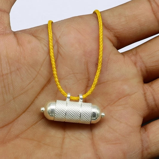 Jupiter remedy silver pendant on a yellow string held in a hand against a white background