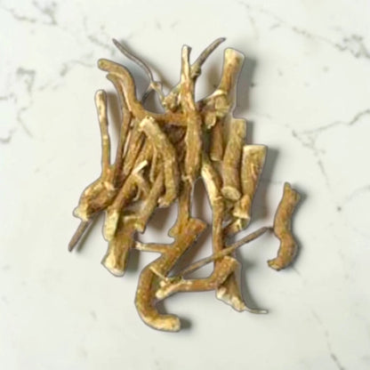 Gold-colored khirni root jadi on a light gray marble surface