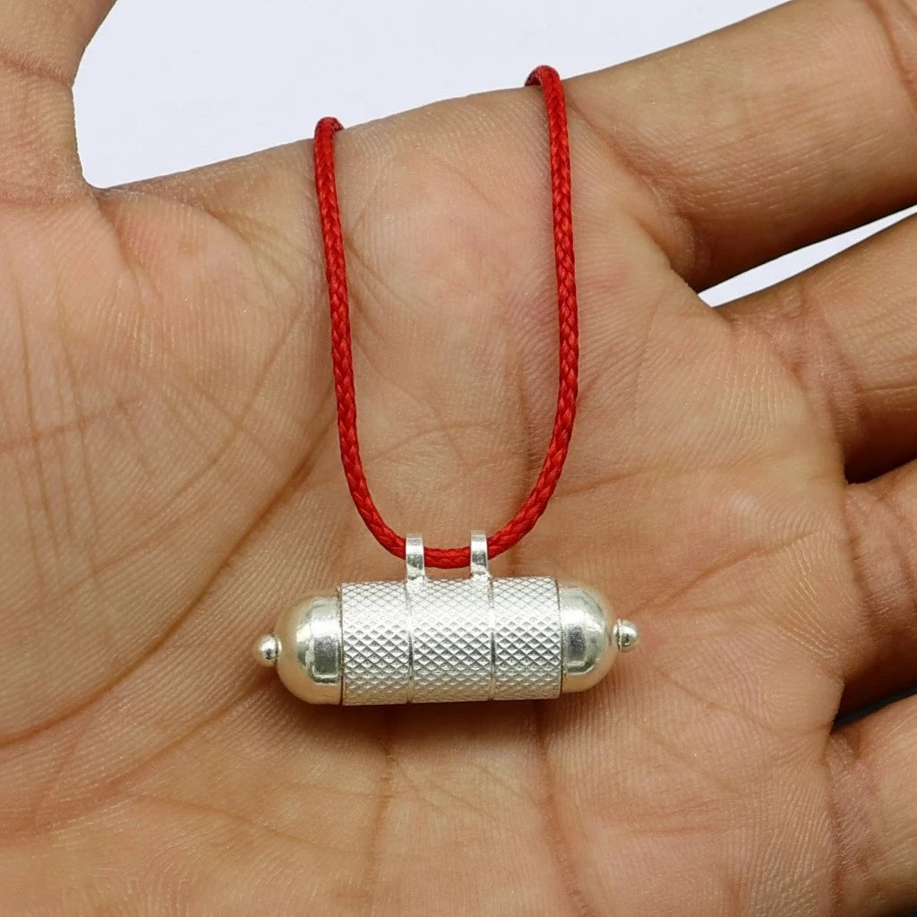 Mars remedy silver pendant on a red string held in a hand against a white background 