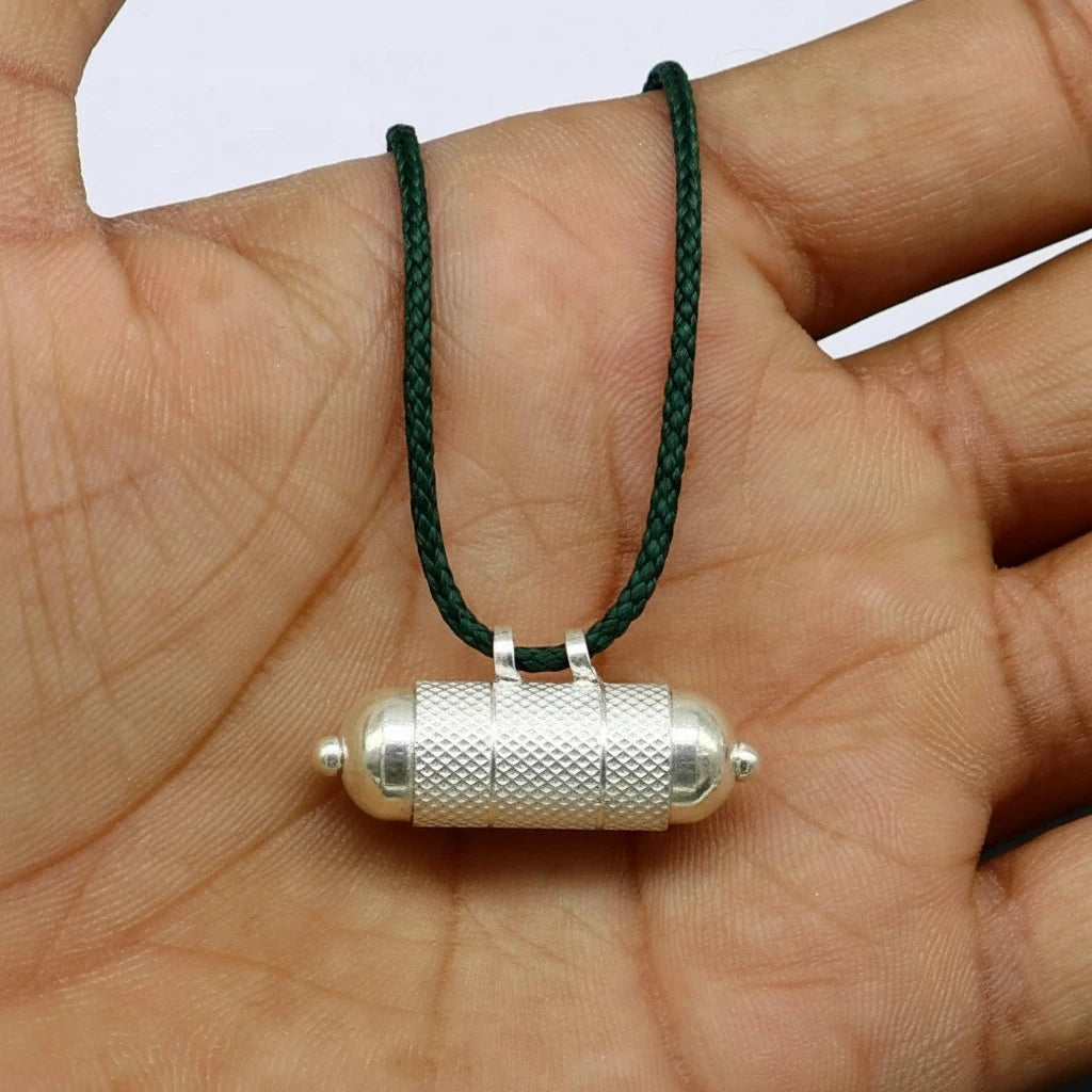 Silver pendant on a green cord held in a hand against a white background as mercury remedy.