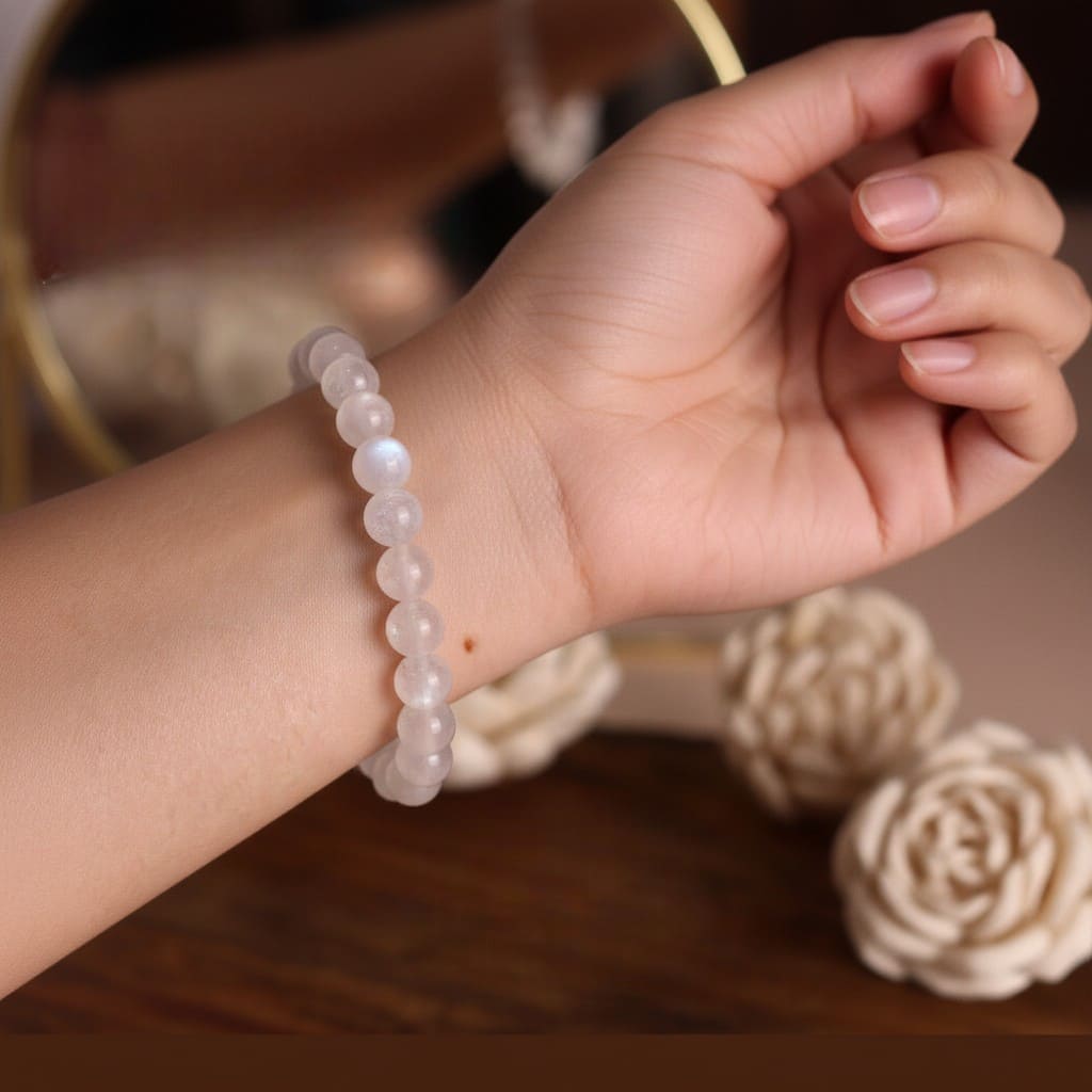 Hand wearing a moonstone bracelet with a blurred floral background