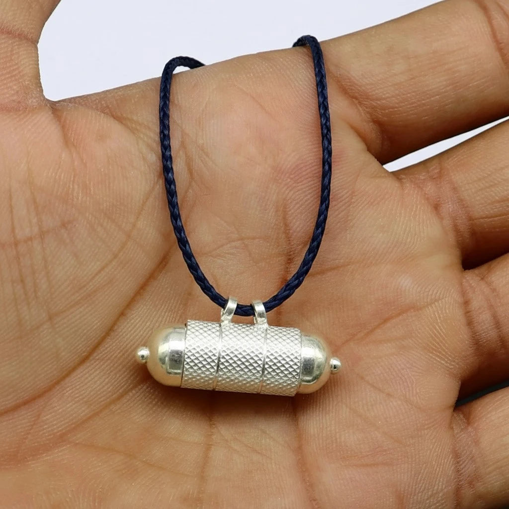 Rahu remedy silver pendant on a dark blue cord held in a hand.