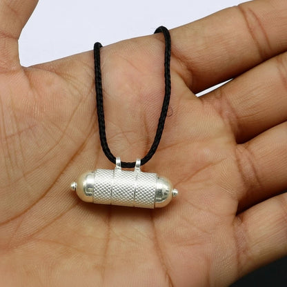 Saturn remedy silver pendant on a black cord held in a hand against a white background