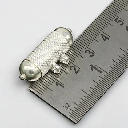 Silver tabiz locket on a metal ruler for measurement