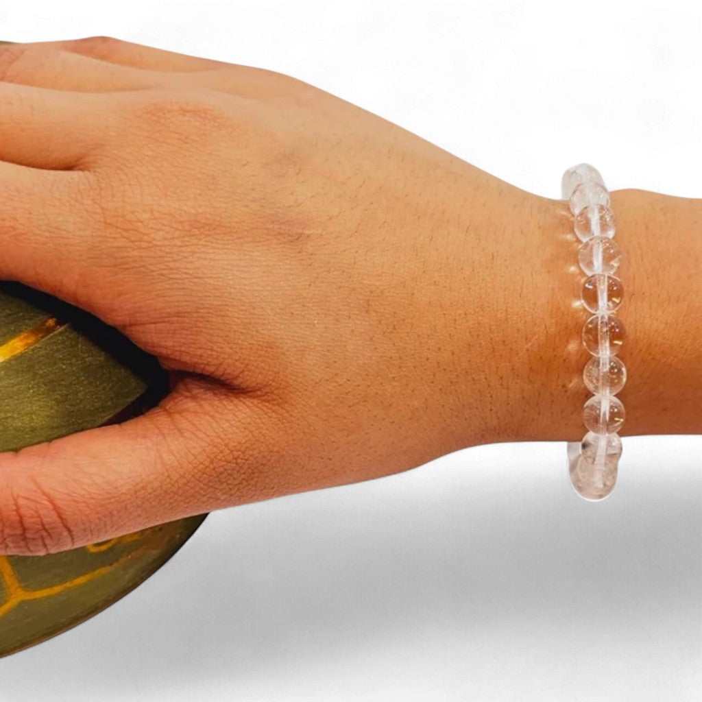 Hand wearing a clear sphatik quartz bracelet on a neutral background