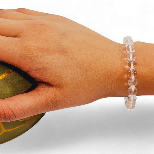 Hand wearing a clear sphatik quartz bracelet on a neutral background