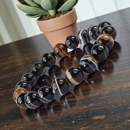 Sulemani Hakik Black and brown beaded bracelet on a wooden surface with a potted plant in the background