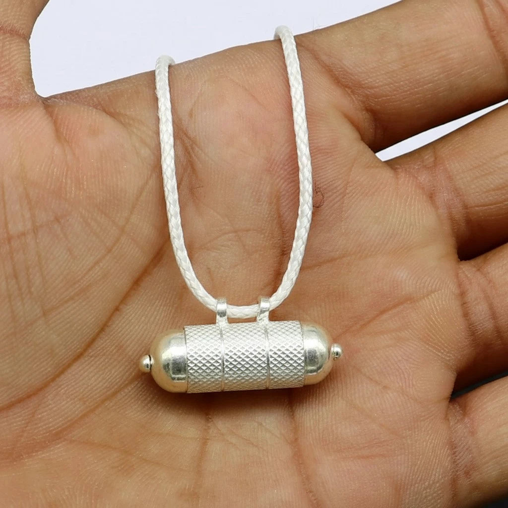 Venus remedy silver cylindrical pendant on a white cord held in a hand.